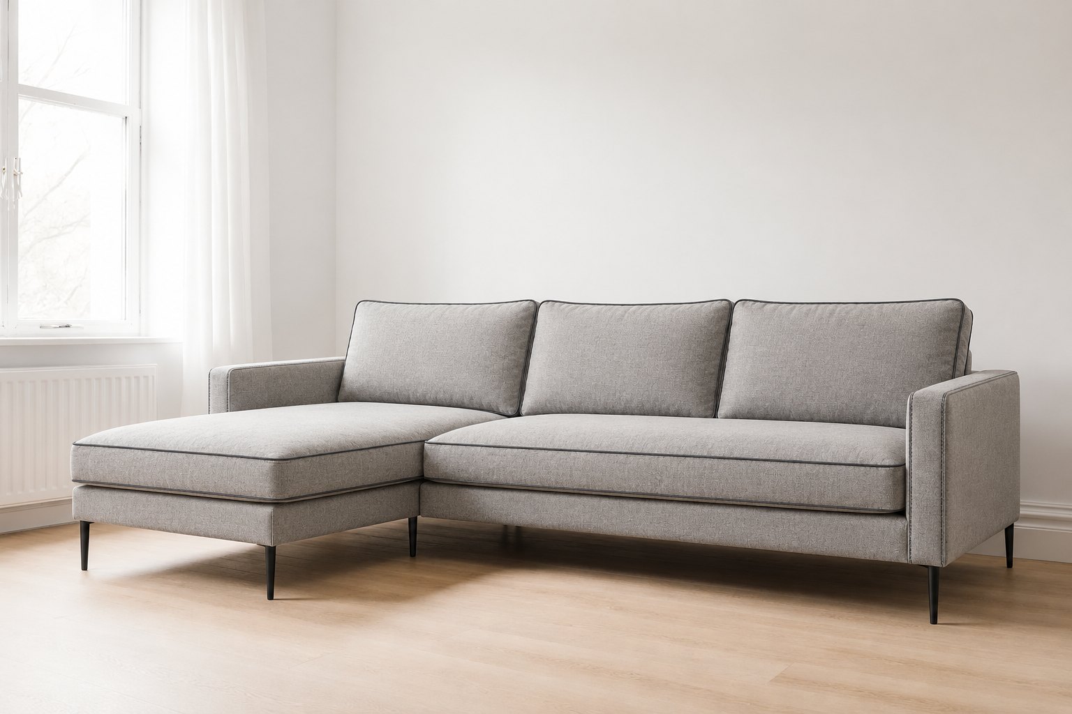 Light grey L-shaped sofa with loose back cushions, charcoal contrast piping, slim arms and matt black legs