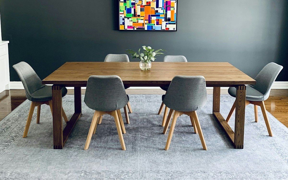 Solid wood dining table on sled-frame legs with six grey upholstered chairs on a pale blue rug